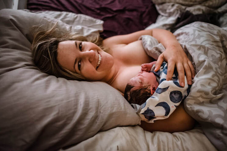 Woman laying down smiling holding newborn baby